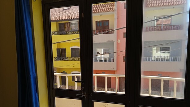 A room with a large window, a blue curtain, and tiled flooring. - Gianni Apartment, Santa Maria, Sal, Cape Verde (Santa Maria)