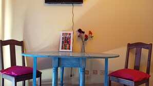 A dining area with a blue table and two wooden chairs with red cushions, a framed picture, and a vase with flowers on the wall. - Gianni Apartment, Santa Maria, Sal, Cape Verde (Santa Maria)