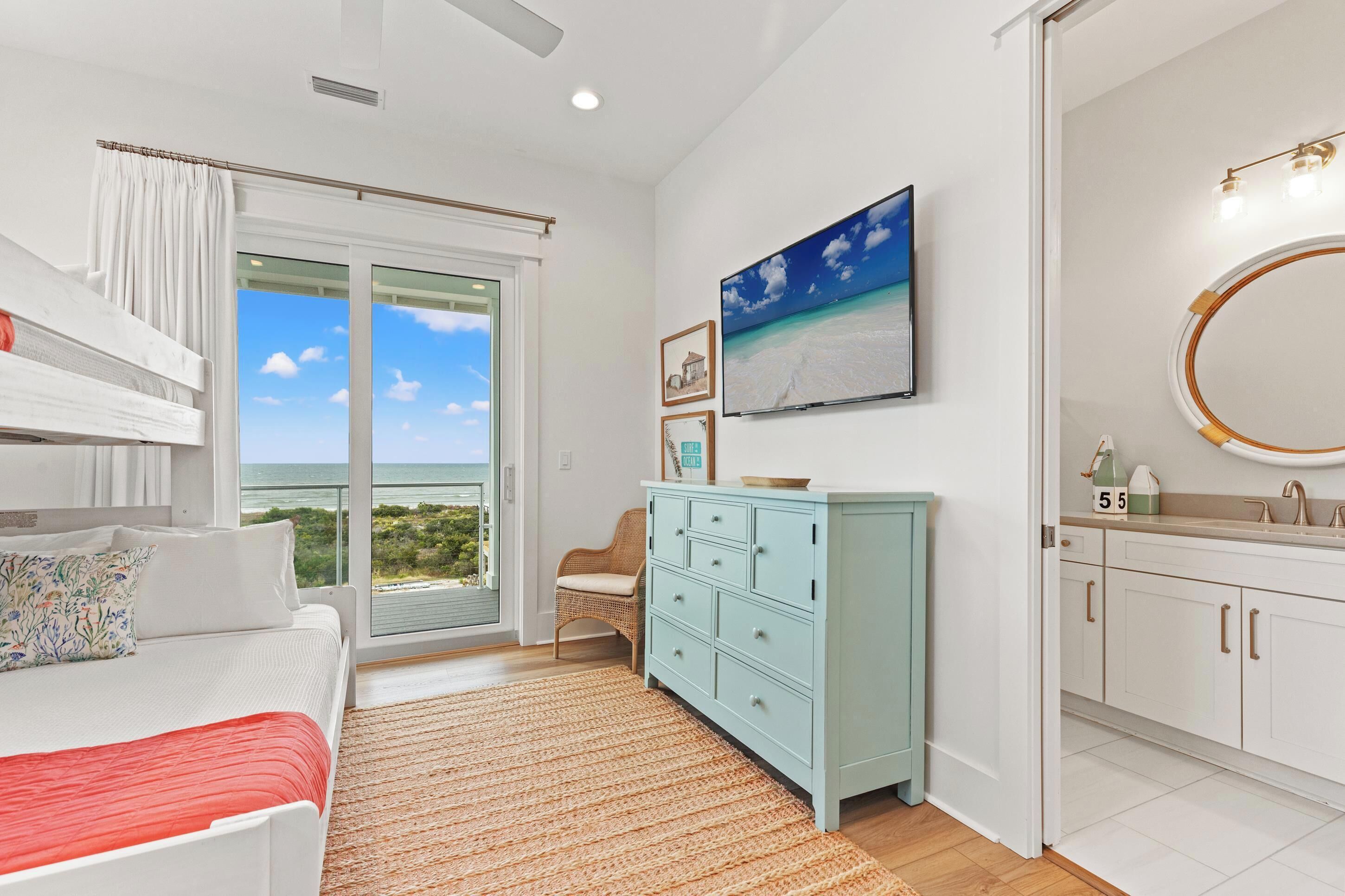 A bedroom with a bed, a dresser, a chair, and a large window with a view of the beach.
