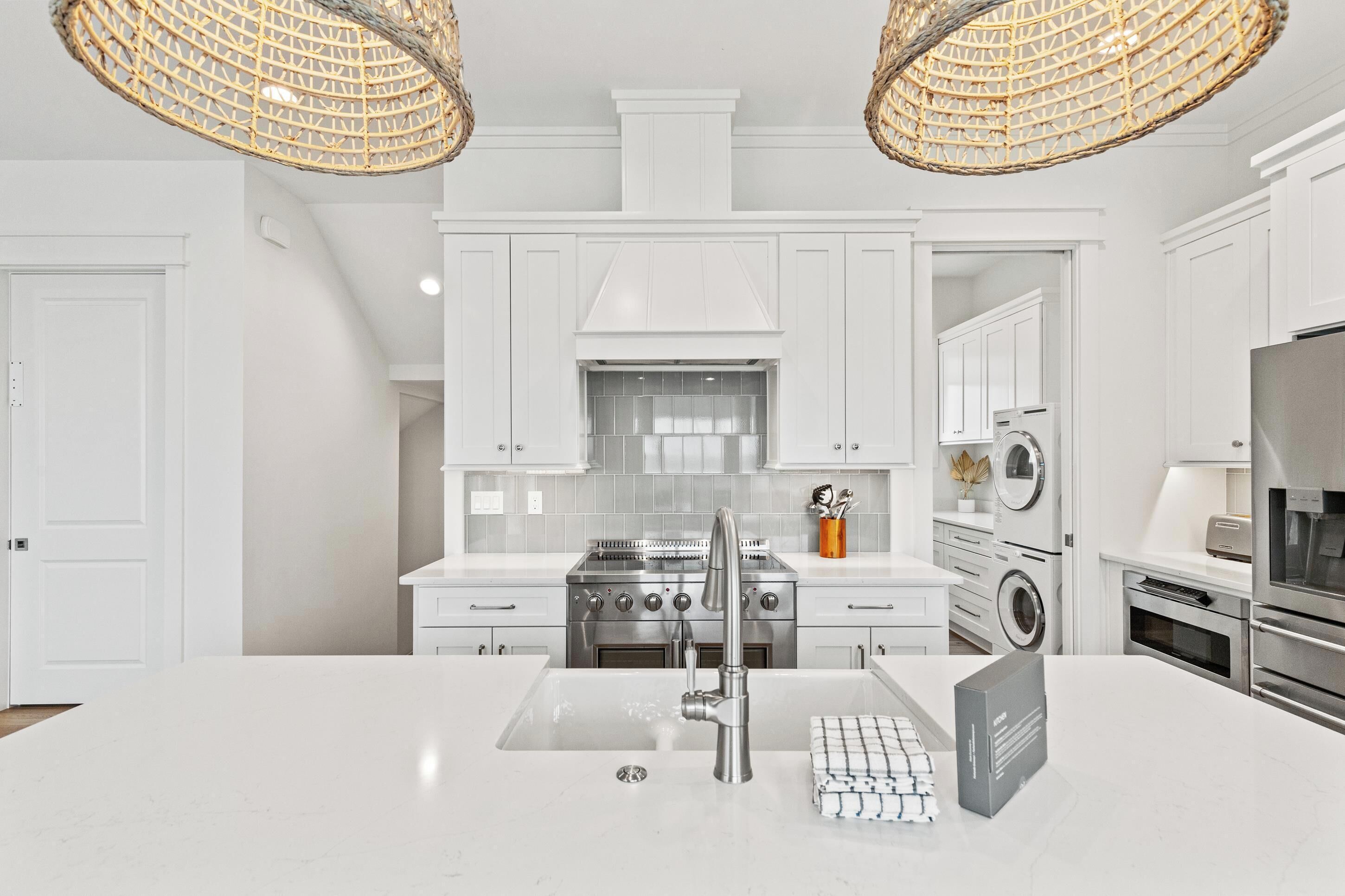A modern kitchen with white cabinetry, a stainless steel stove, a built-in oven, a sink with a modern faucet, and a large island.