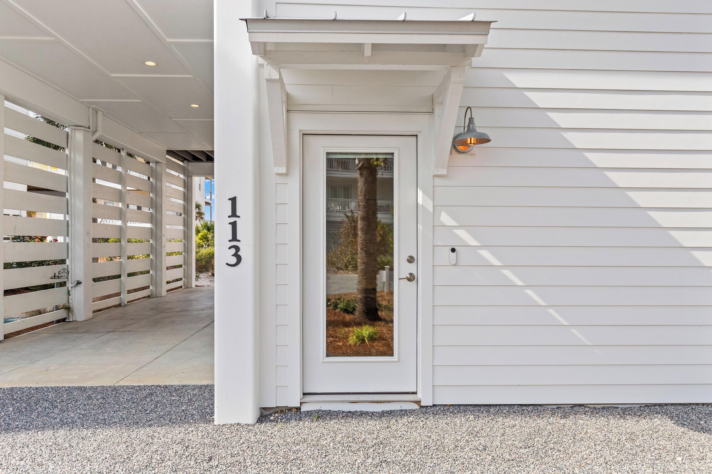 A white building with a number 113 on the door, a covered entrance, and a small garden visible through the door.