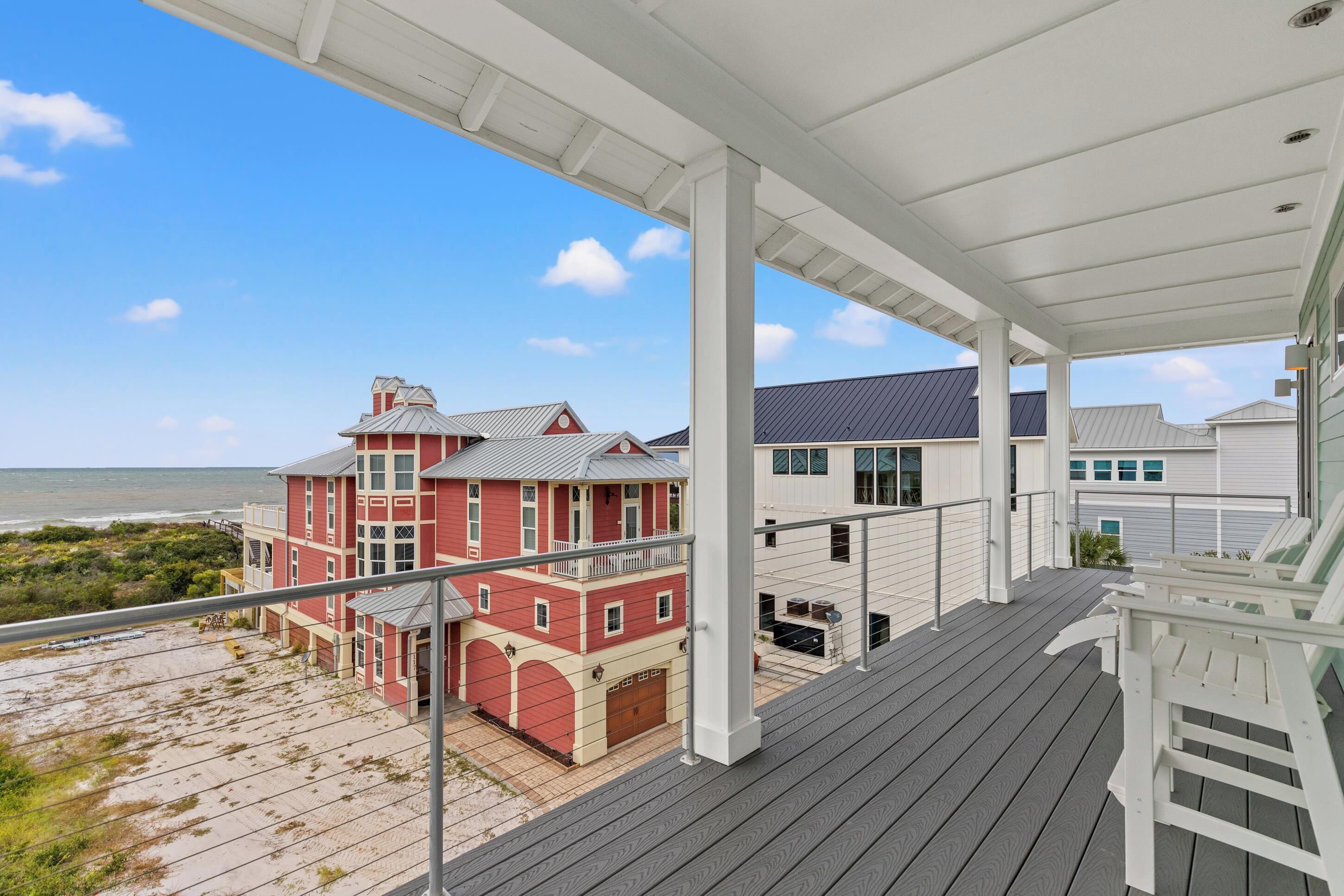 A covered balcony with a view of a red house and beach.