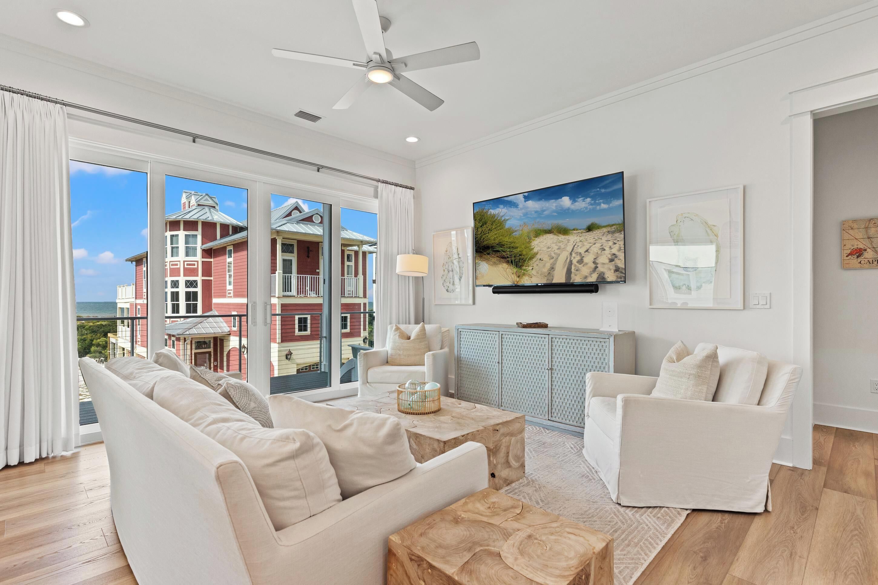 A spacious living room with a large window, a ceiling fan, and a view of a red building.