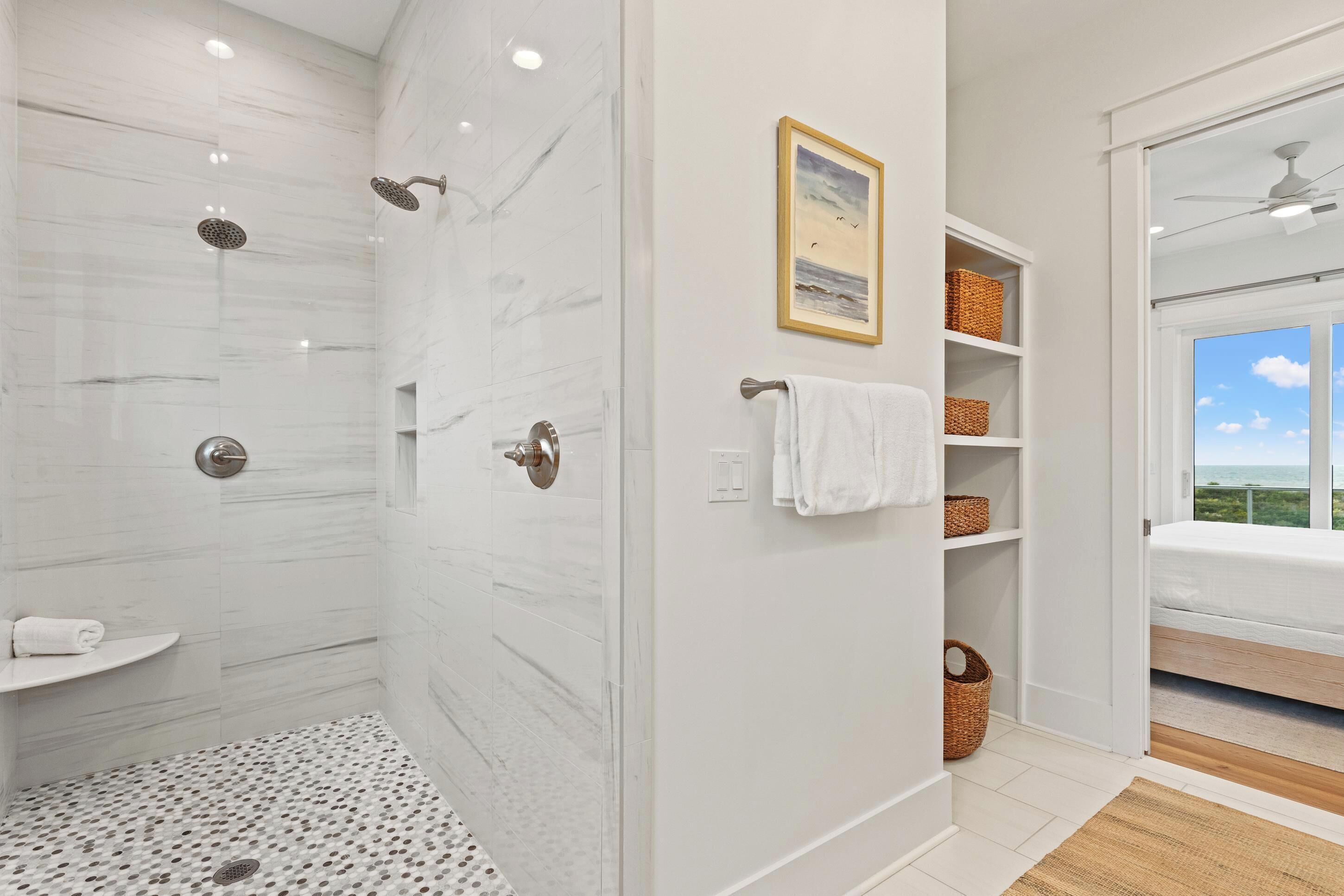 A modern bathroom with a walk-in shower, white marble walls, and a view of the outdoors through a window.