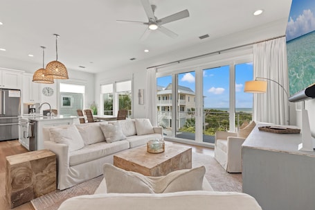 A spacious living area with a large sofa, a coffee table, and a view of the ocean through large sliding doors.