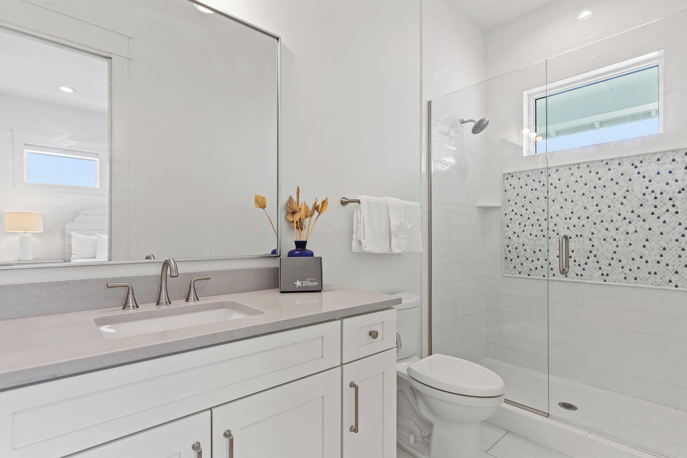 Une salle de bain moderne avec un grand miroir, un lavabo, des toilettes et une douche à parois de verre.