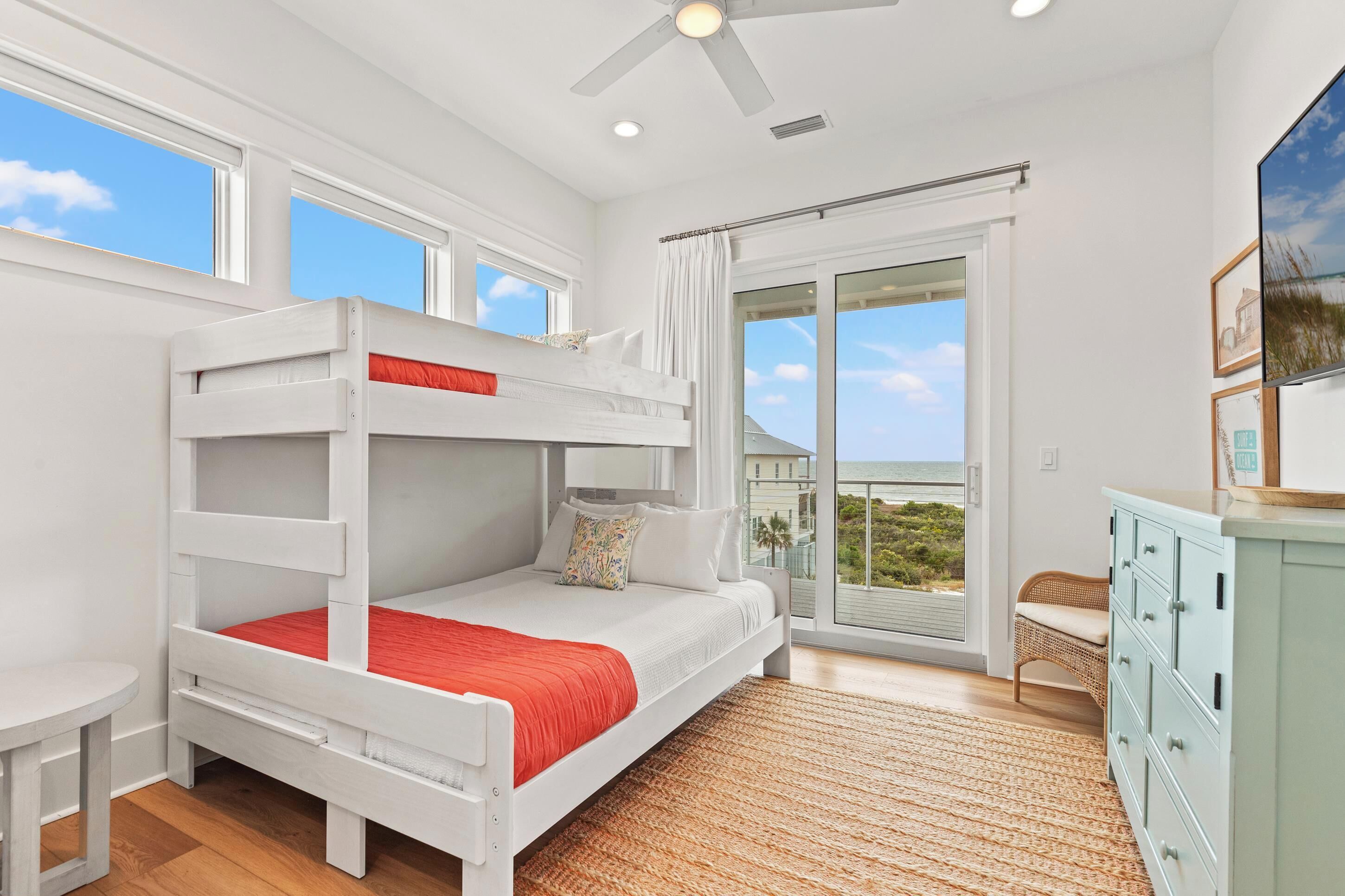 A bunk bed with a red mattress, a small table, and a wicker chair.