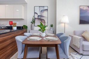 Een moderne eetruimte met een houten tafel gedekt voor vier personen, omringd door lichtblauwe stoelen. Er staan potplanten op de tafel en een schilderij erboven.