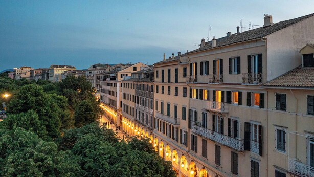 Una hilera de edificios históricos con balcones y una calle arbolada.