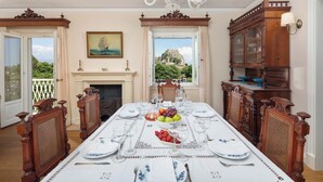 Un comedor con una gran mesa dispuesta para una comida, una chimenea y vistas a una colina con un castillo.