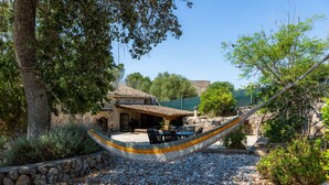 A hammock in a garden with a stone wall, a patio with outdoor furniture, and a building with a tiled roof in the background. - Can Gallot De Punxuat – Mountain Views, Private Pool, Wi-Fi & Air Conditioning (Algaida)