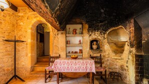 A stone-walled room with a table set for two, a shelf with pottery, and a fireplace. - Can Gallot De Punxuat – Mountain Views, Private Pool, Wi-Fi & Air Conditioning (Algaida)