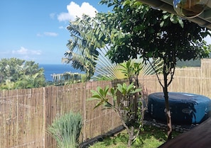 A bamboo fence, a small tree, and a blue water heater in a backyard with a view of the ocean.
