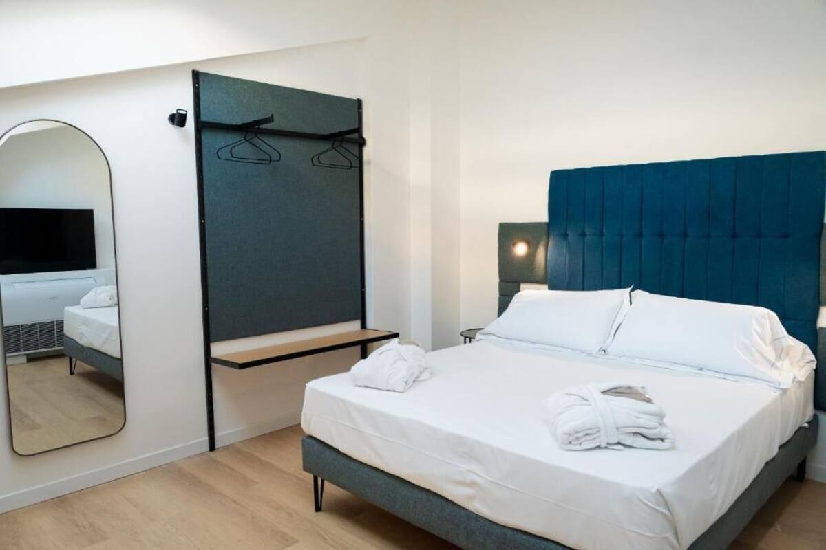 Una habitación de hotel moderna con una cama grande, una mesita de noche, un espejo y un armario.