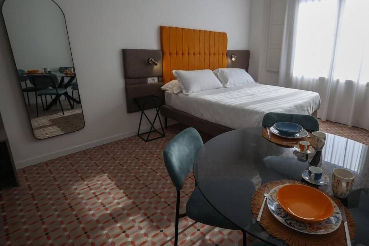 Habitación de hotel con cama, una mesa de comedor con sillas, un espejo y una ventana con cortinas.