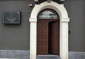 Entrada a un hotel-apartamento con un cartel sobre la puerta, un arco blanco y una pared oscura.