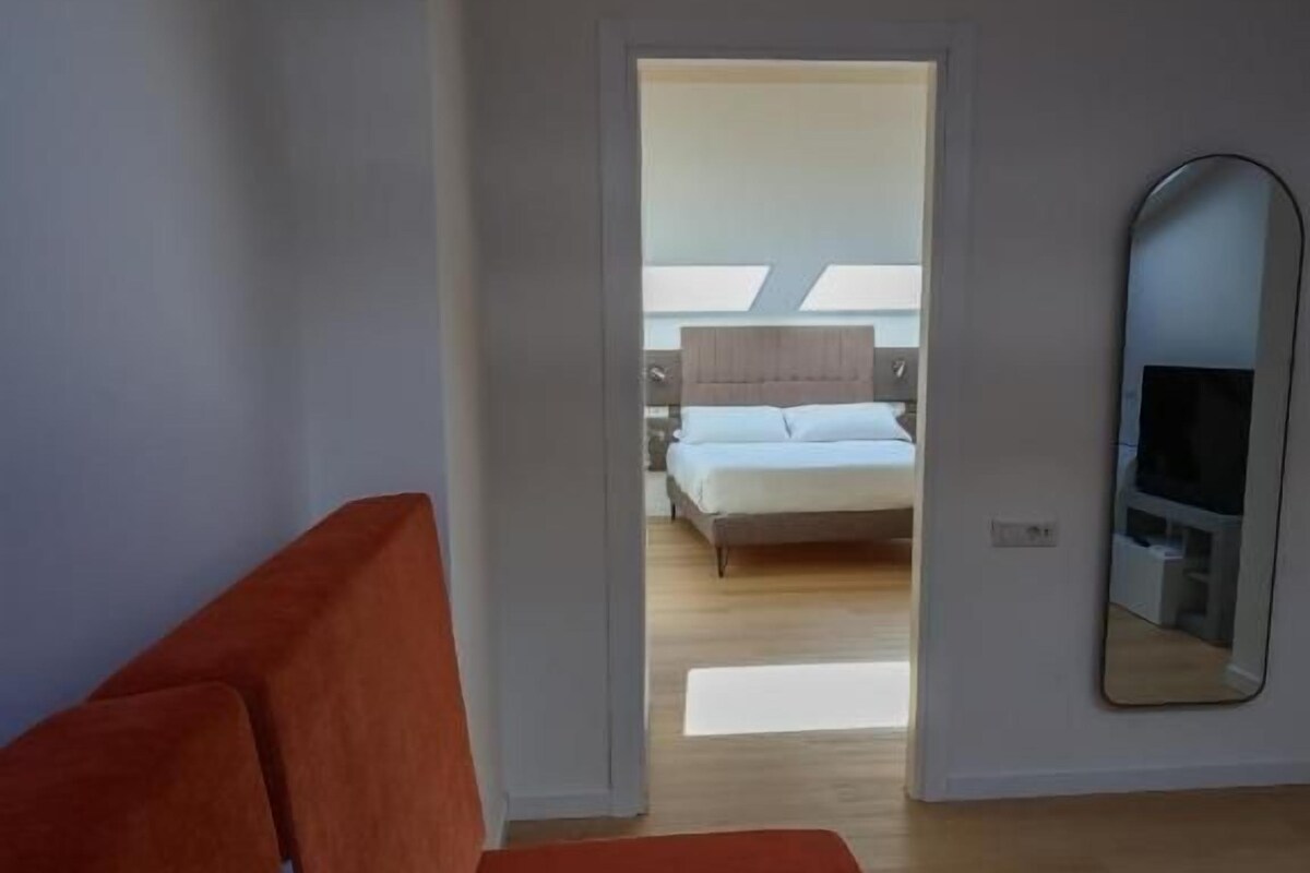 A modern bedroom with a large bed, a red sofa, and a TV.