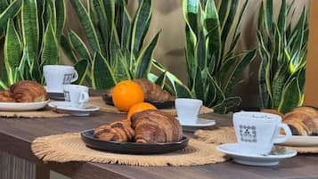 A breakfast table with croissants, orange, and coffee cups.