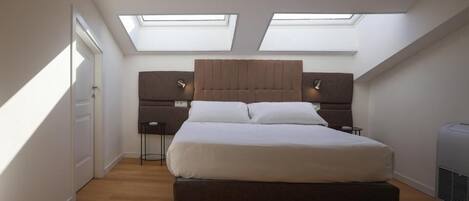 Un dormitorio con cama, dos mesitas de noche, cabecera y tragaluces.