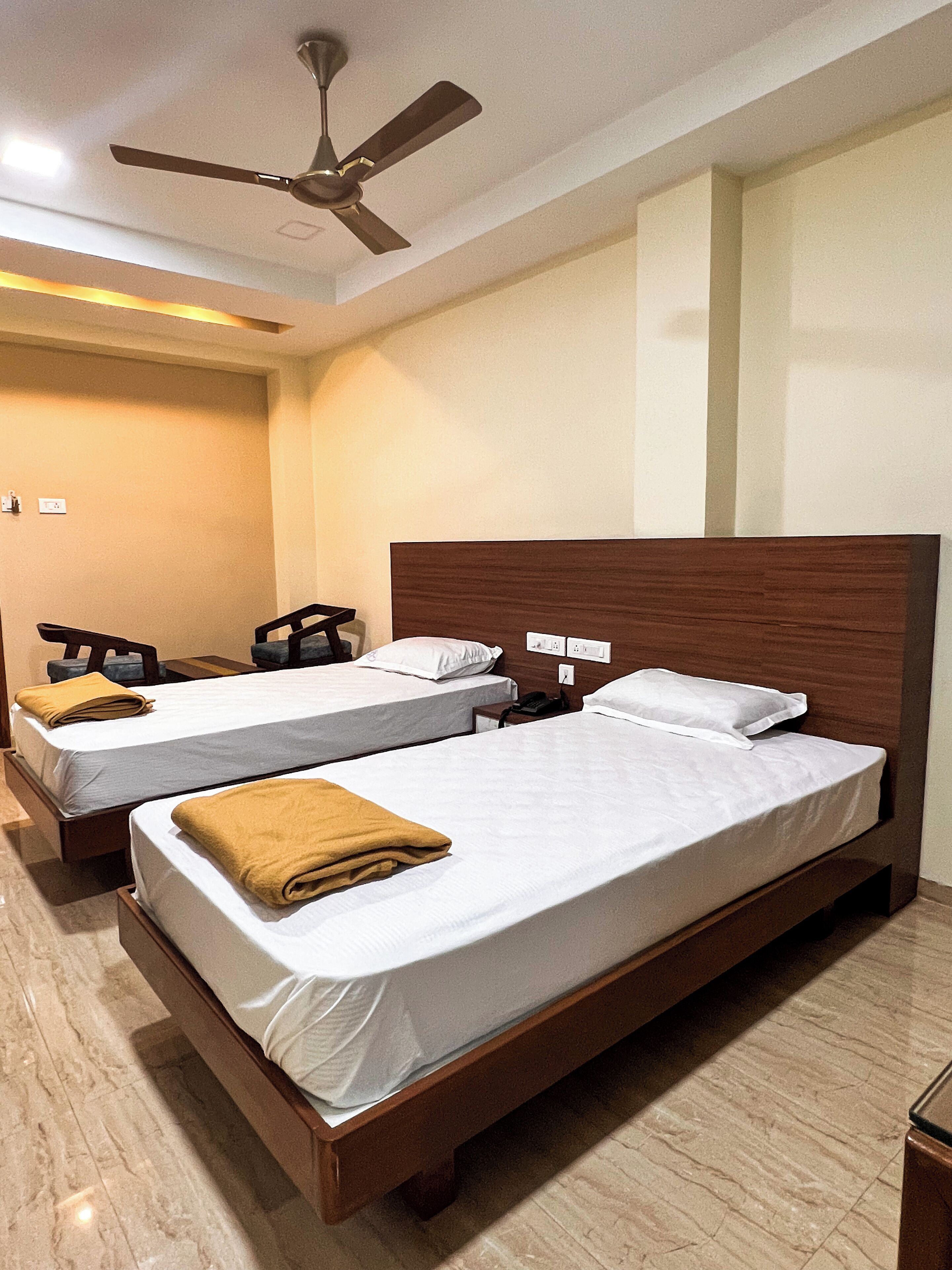 A hotel room with two single beds, a ceiling fan, and a marble floor.