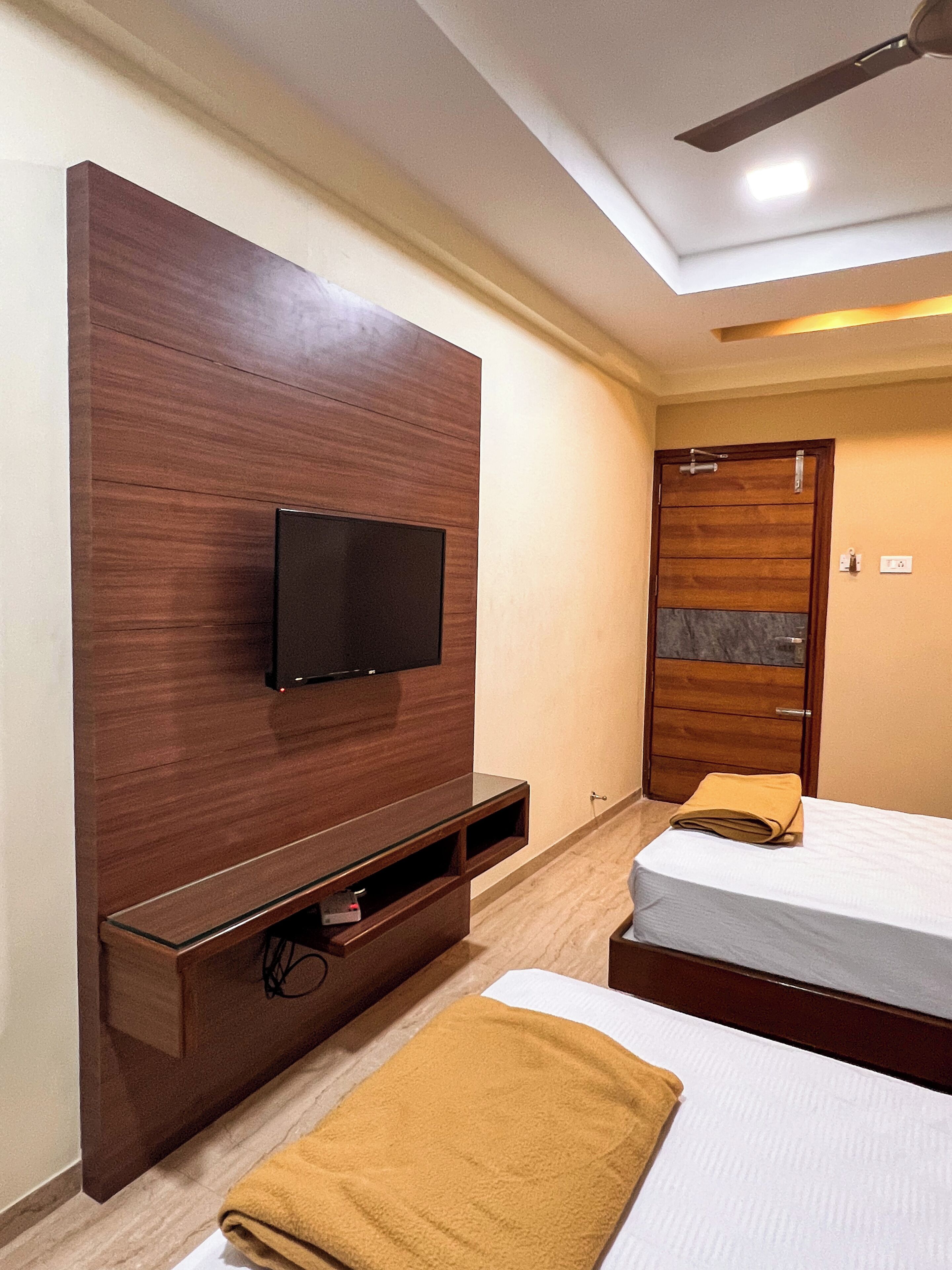 Habitación de hotel con pared de madera decorativa, televisor de pantalla plana, cama con colchón blanco y toalla amarilla, y armario de madera con espejo.