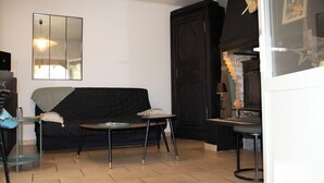 Un salon avec un canapé noir, une petite table ronde, un miroir au mur et une cheminée.