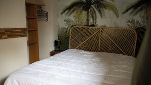 Un lit avec une tête de lit en osier, une étagère en bois et une fresque murale représentant des palmiers.
