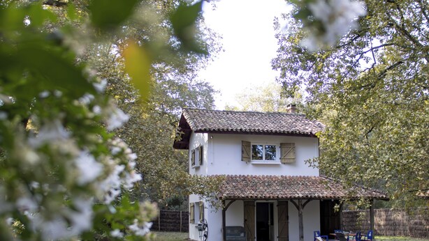 Une maison à deux étages, avec un toit en tuiles, une terrasse couverte et un jardin.