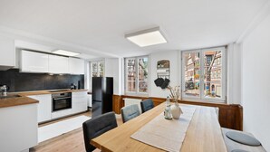 A modern kitchen with white cabinets, a wooden countertop, and a built-in oven. There is a dining area with a wooden table and chairs, and large windows with a view of traditional buildings. - Half-timbered apartment Calw - vacation in the picturesque and historic old town (Calw)