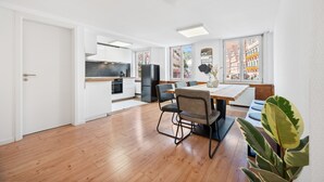 A spacious kitchen with modern appliances, a dining area with a wooden table and chairs, and large windows offering a view of colorful buildings. - Half-timbered apartment Calw - vacation in the picturesque and historic old town (Calw)