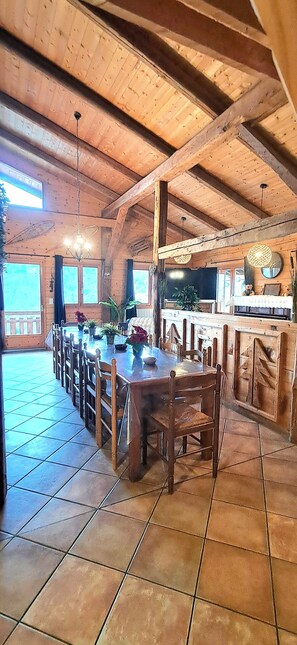 A rustic wooden dining area with a long table and chairs, a kitchen area with a sink and countertop, and large windows providing natural light. - Le lodge des ours Located just a few minutes from the Espace Diamant, with sublime views. (Cohennoz)