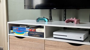 A white entertainment unit with a flat-screen TV, two game controllers, and a white gaming console.