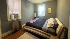 A bedroom with a bed, a ceiling fan, a radiator, and a window with curtains.