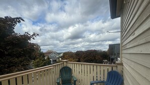 A wooden deck with two chairs, a railing, and a view of houses and trees under a cloudy sky.