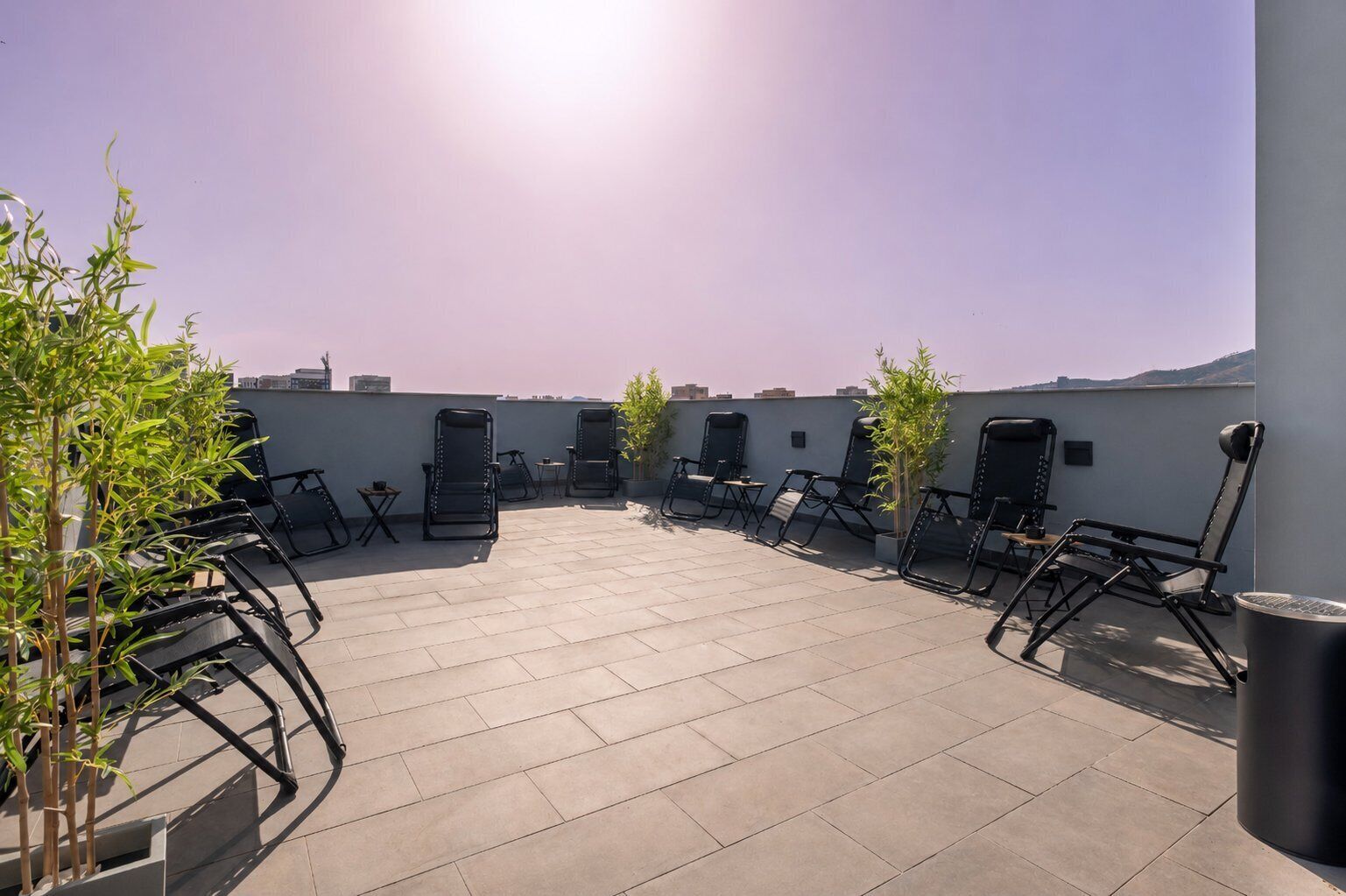 Um terraço no telhado com várias cadeiras de lounge pretas, uma mesinha e vasos de plantas.