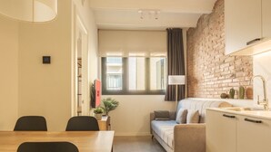 Een ruimtelijk ingerichte leefruimte met een eethoek, een bank, een kitchenette en een bakstenen muur.