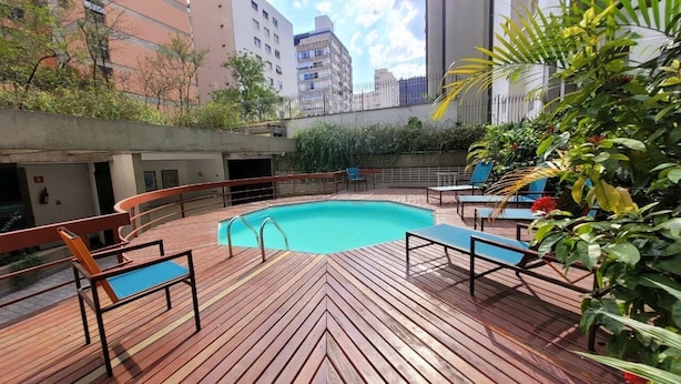 A rooftop pool area with wooden deck, lounge chairs, and a view of surrounding buildings. - Lorena 1157 (São Paulo)