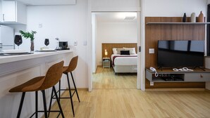 A modern hotel room with a kitchen area, a bed with a wooden headboard, a TV, and a small desk with a telephone. - Lorena 1157 (São Paulo)