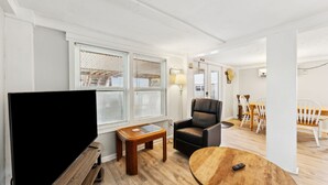 Un soggiorno moderno con una TV a schermo piatto, un tavolino in legno, una poltrona in pelle e una zona pranzo con sedie e tavolo in legno.