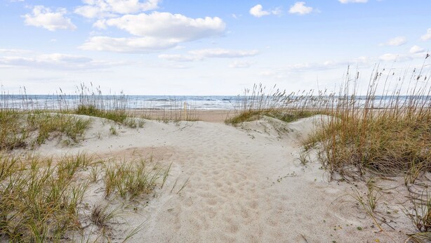 Un sentiero sabbioso che conduce al mare, circondato da erba e dune.