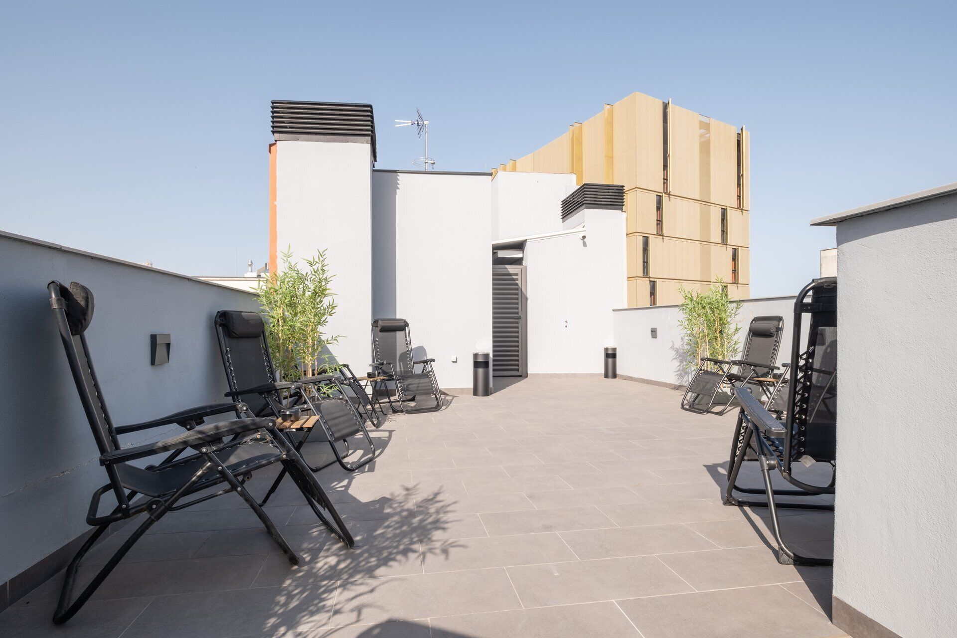 Eine Dachterrasse mit Außenmöbeln, ein Gebäudeeingang und ein klarer Himmel.