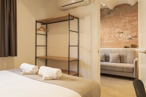 Een slaapkamer met een bed, een houten wandplank, een grijze bank en een bakstenen muur.
