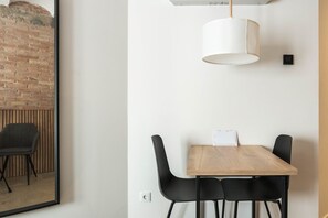 A modern dining area with a wooden table, black chairs, a white pendant light, and a brick wall. - Guest Ready - Fira Barcelona Modern Studio (L'Hospitalet de Llobregat)