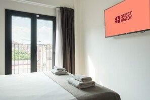 Een hotelkamer met een bed, een raam met gordijnen, uitzicht op gebouwen en een bord met de tekst 'GUEST READY' aan de muur.