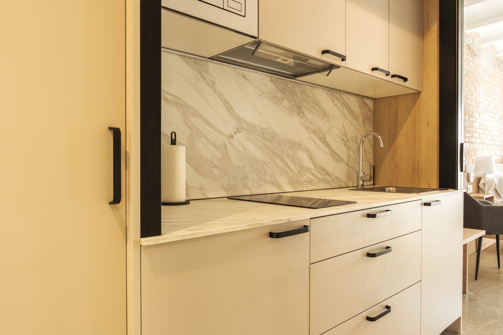 A modern kitchen with a marble backsplash, a stainless steel sink, and a black faucet.