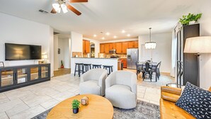 A modern living room with a TV, sofa, and coffee table. There is a kitchen area with a dining table and chairs.
