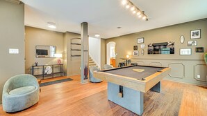 A pool table in a room with wooden flooring, a grey armchair, and a staircase leading to another level.