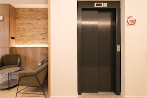 A modern elevator with a digital display, a 'No Smoking' sign, and a brick wall with wooden paneling. - Guest Ready - Fira Barcelona Modern Studio (L'Hospitalet de Llobregat)