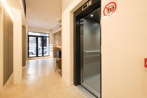 Un passadís amb una porta de vidre, un senyalitzador que indica prohibició de fumar i vista de cotxes aparcats a l'exterior.