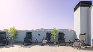 A rooftop terrace with several reclining chairs, potted plants, and a view of distant buildings. - Guest Ready - Fira Barcelona Modern Studio (L'Hospitalet de Llobregat)